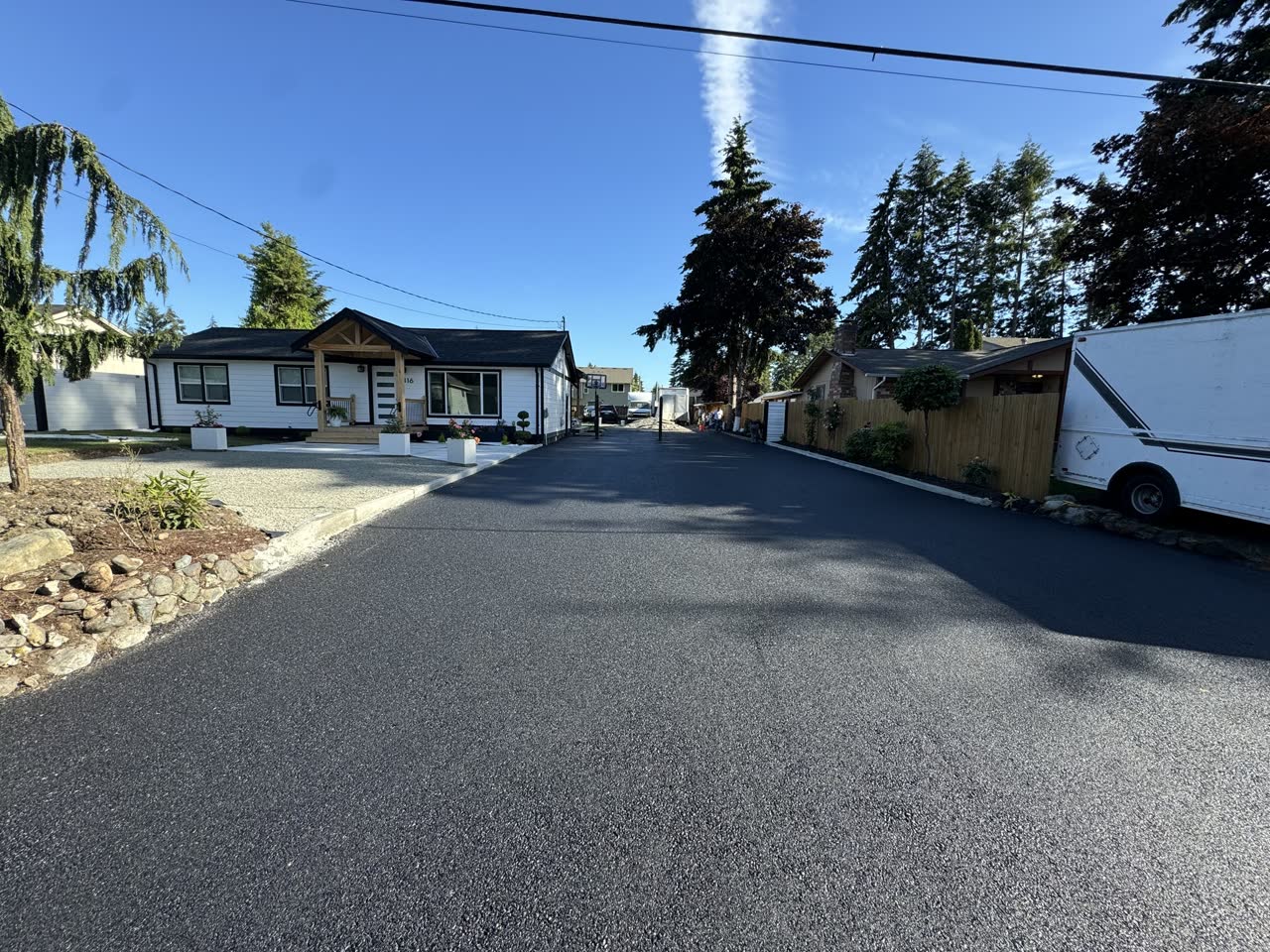 Long sunny asphalt driveway lined with evergreens